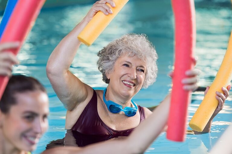 Woman enjoying an aqua fitness program for seniors with swim noodles in a pool.