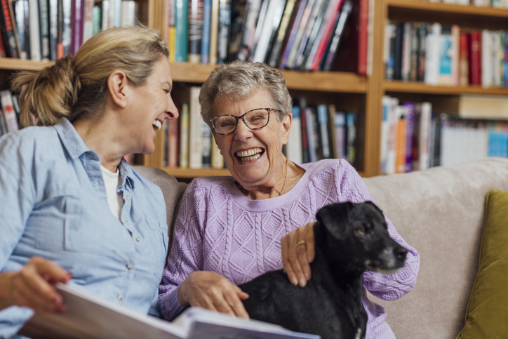 Senior woman daughter and black dog laughing on a couch by a bookshelf