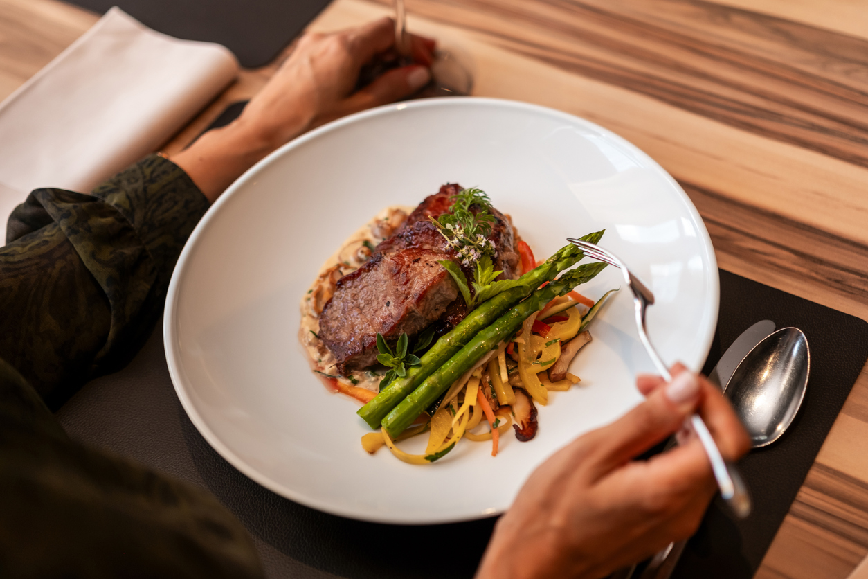 Gourmet steak and asparagus dish on a white plate being eaten