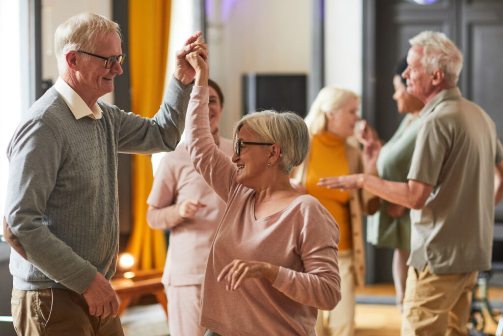 Senior couple dancing happily in a room with other seniors