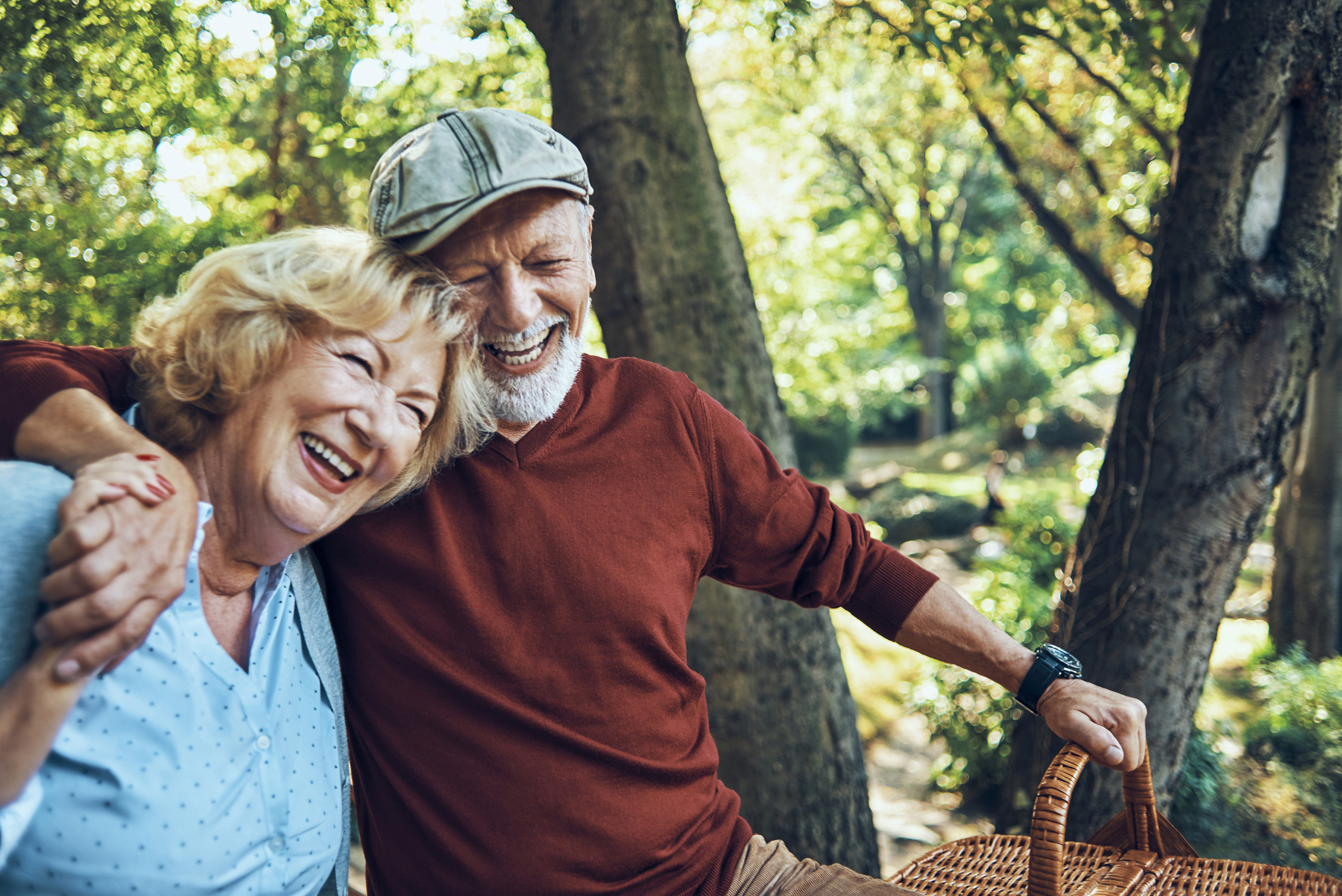 Joyful senior couple embracing and laughing outdoors with a picnic basket