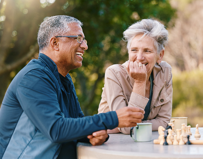 Two seniors laughing while playing chess outdoors