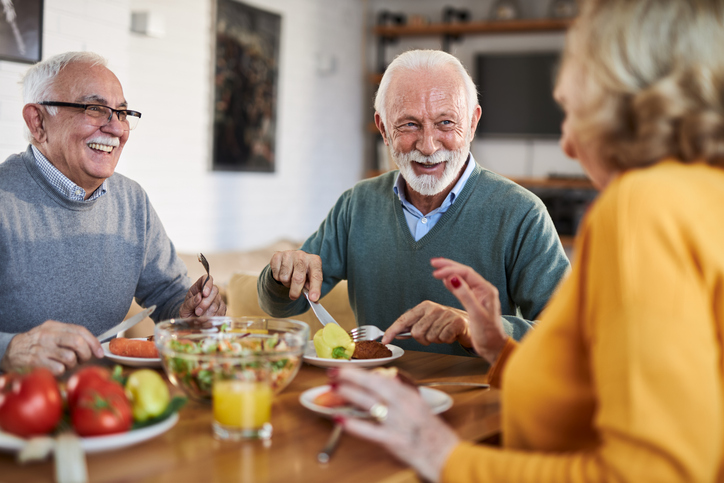 Three smiling seniors enjoying a healthy meal together at a table