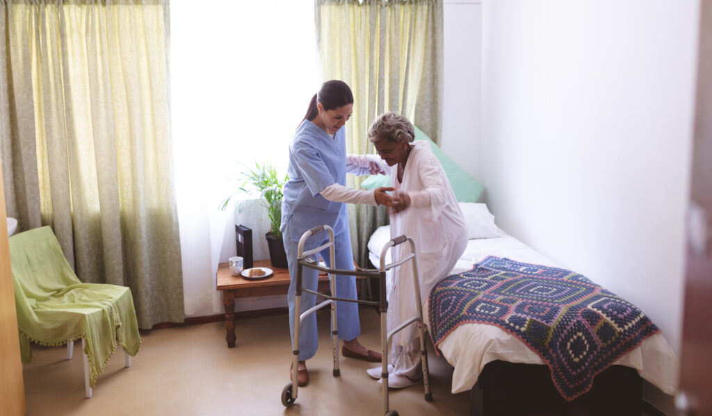 Caregiver helping a senior woman with a walker get out of bed