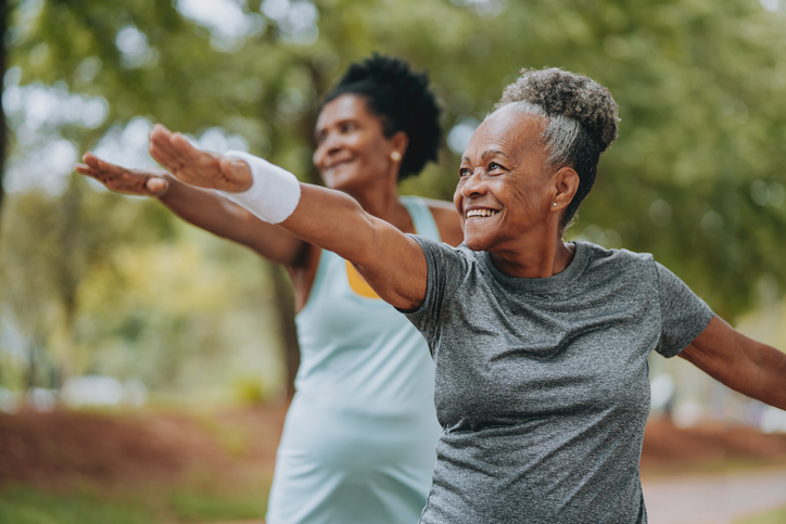 Two senior women smiling while doing outdoor yoga in a park