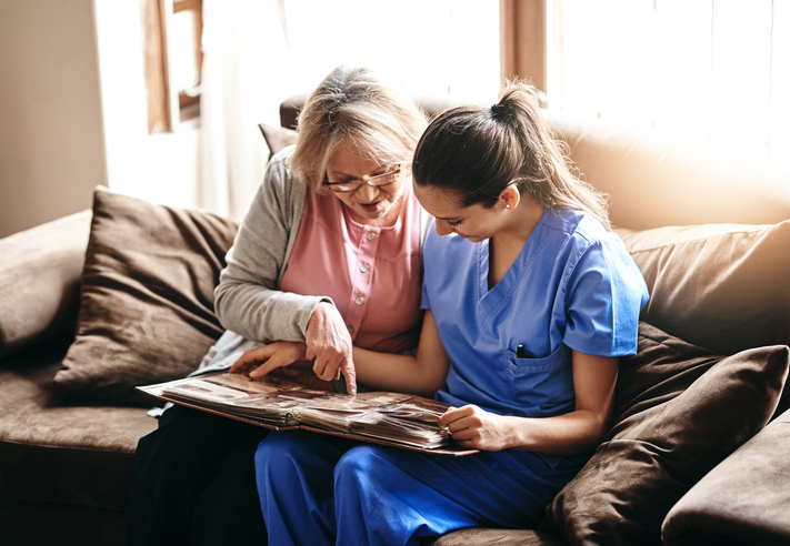 Caregiver and senior woman looking at a photo album on a couch