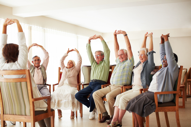 Group of seniors doing seated arm exercises in a bright room